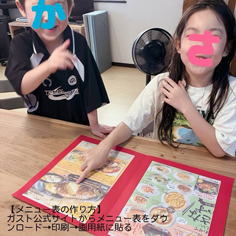 手作りメニュー表を見ながらハンバーグを指さす女の子とその横で笑っている男の子
