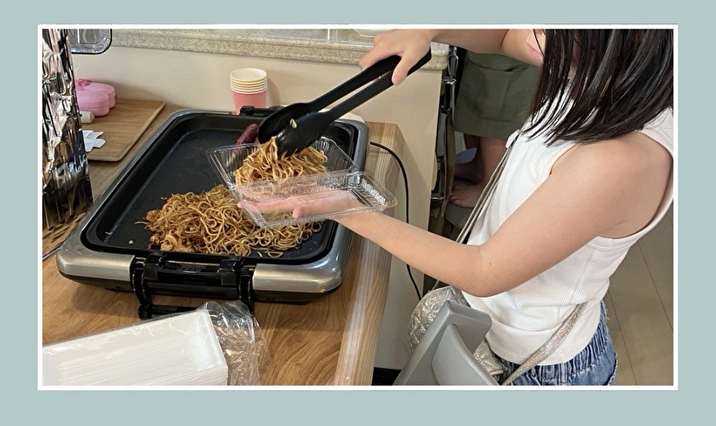 ホットプレートから焼きそばをパックに移し入れようとしている女の子